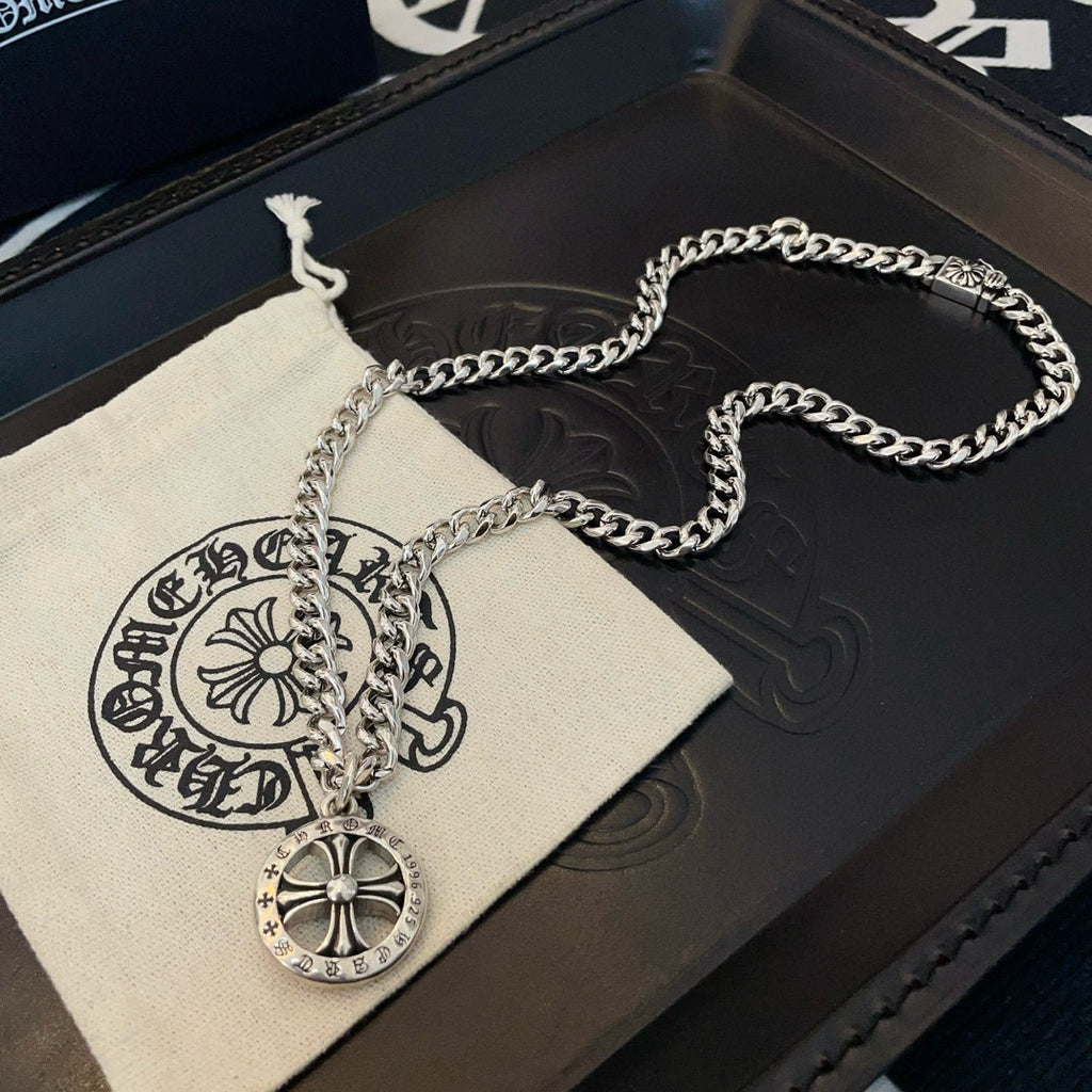 Silver-toned chain necklace with round compass pendant on a dark box and pouch