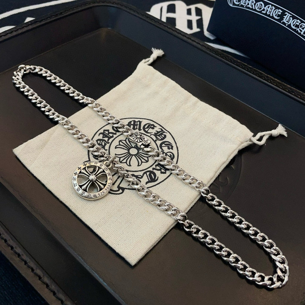 Silver-toned chain necklace with round compass pendant on a white branded pouch