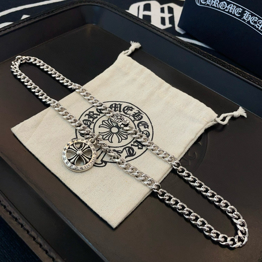 Silver-toned chain necklace with round compass pendant on a white branded pouch