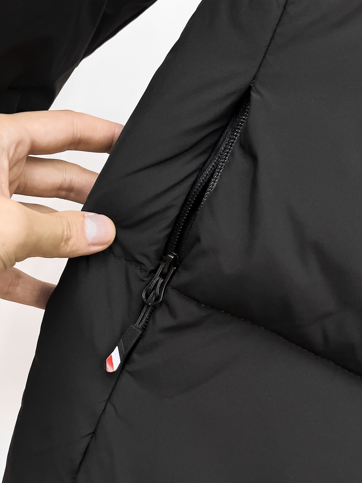 Puffer jacket with black zipper and side seam detail, shown with finger