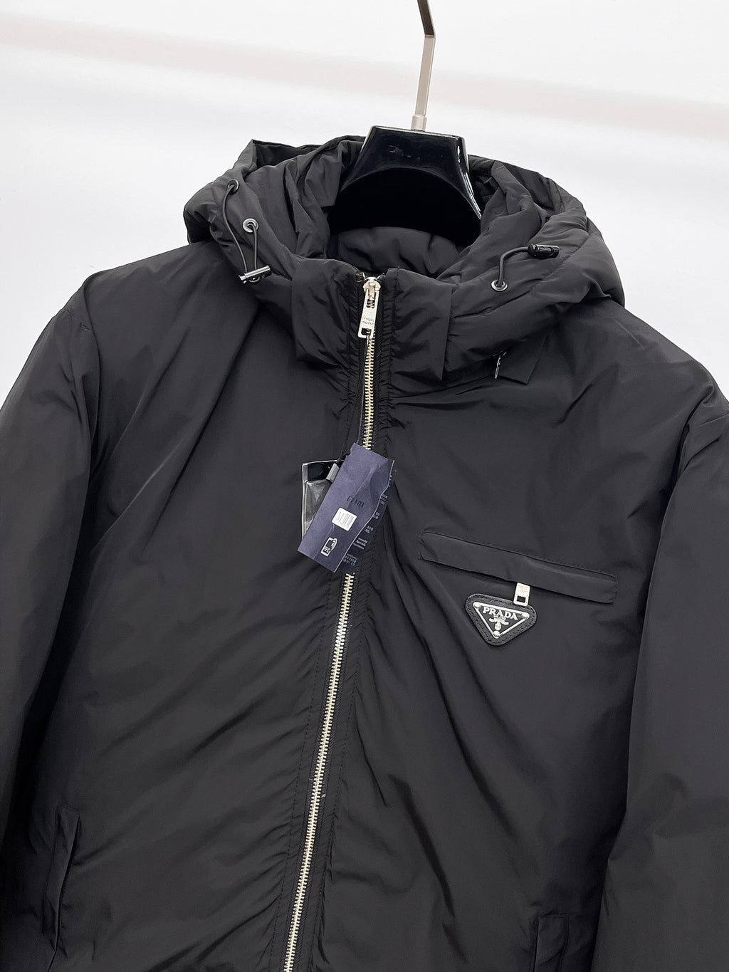 Close-up of black hooded puffer jacket with front zipper and triangular logo badge