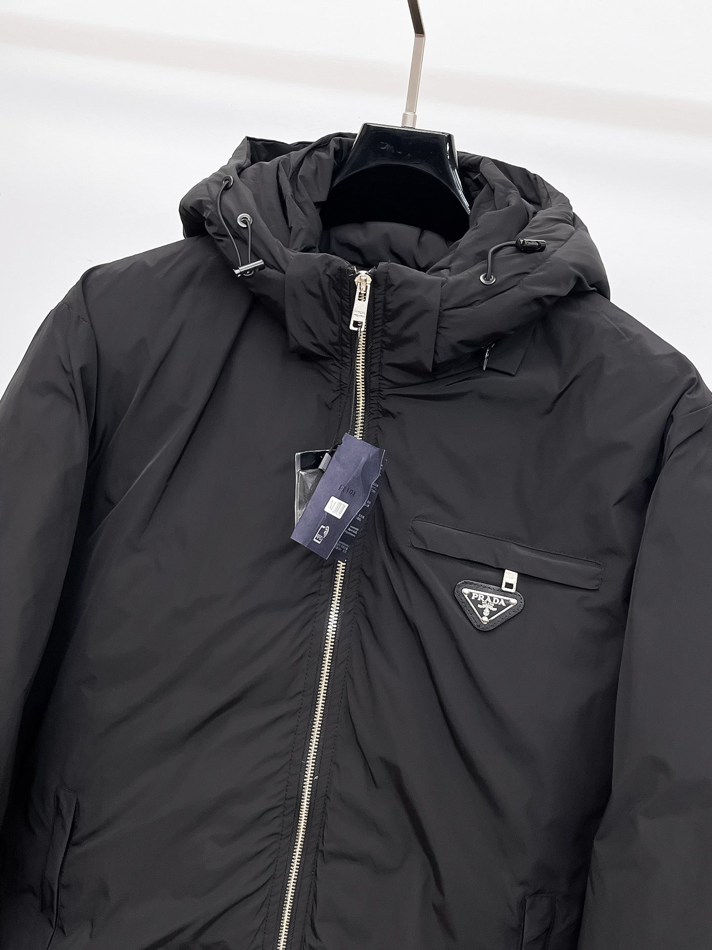 Close-up of black hooded puffer jacket with front zipper and triangular logo badge
