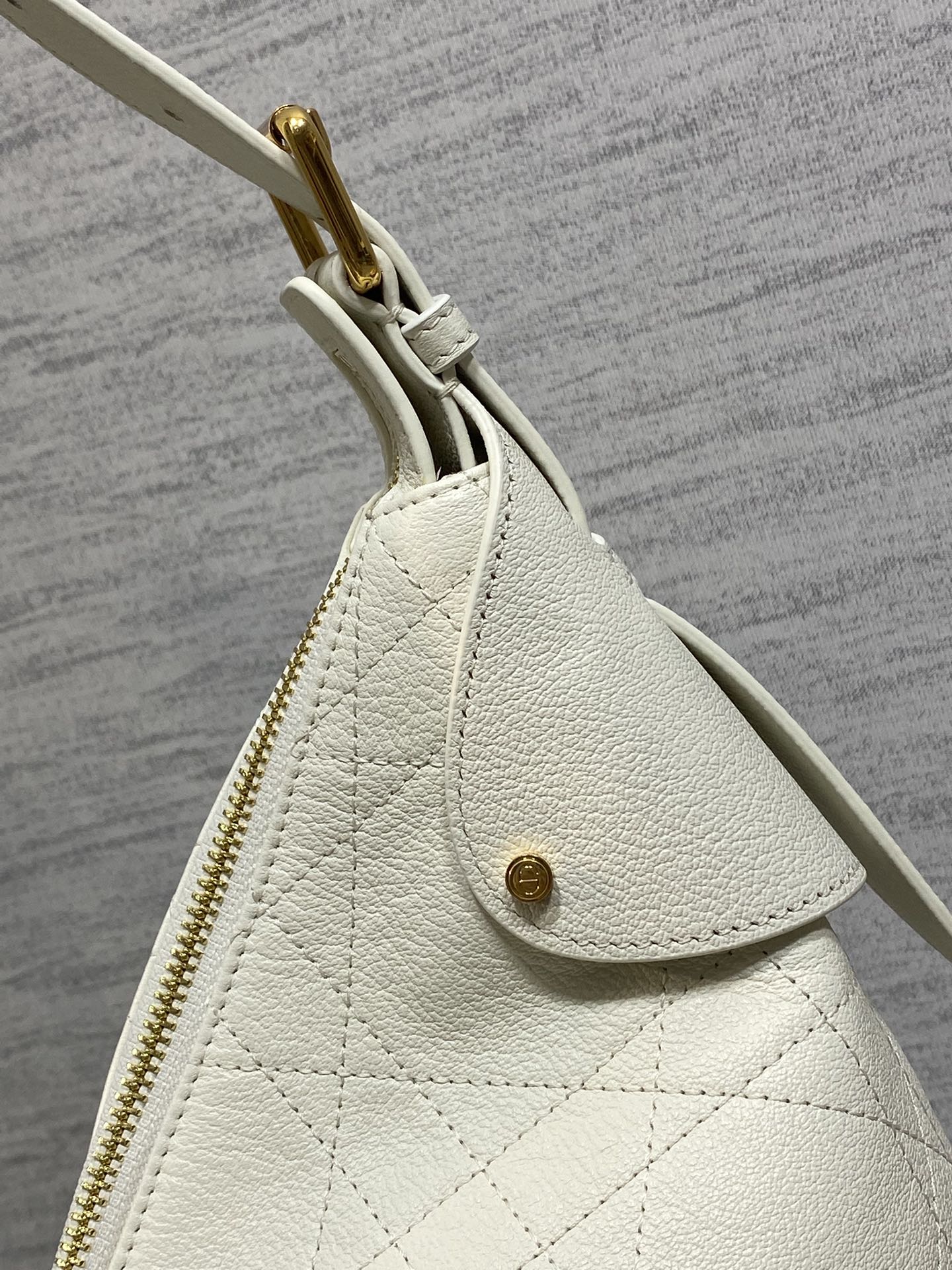 Dior bag side view with gold zipper pull, white leather and small charm