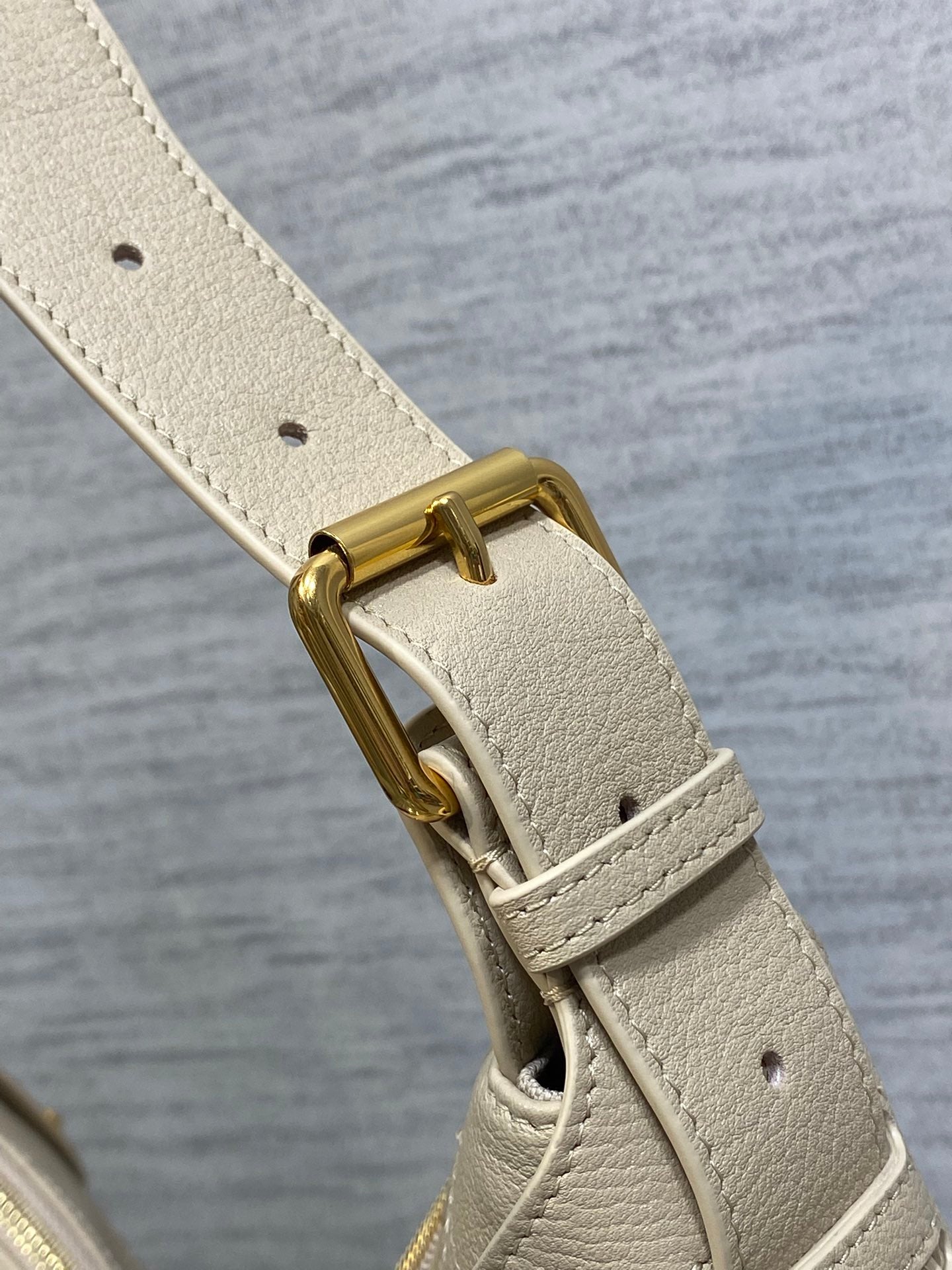 Cream leather shoulder strap with gold-tone buckle hardware and punched eyelets.