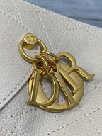 Gold hardware charm on cream quilted leather bag with “D” emblem