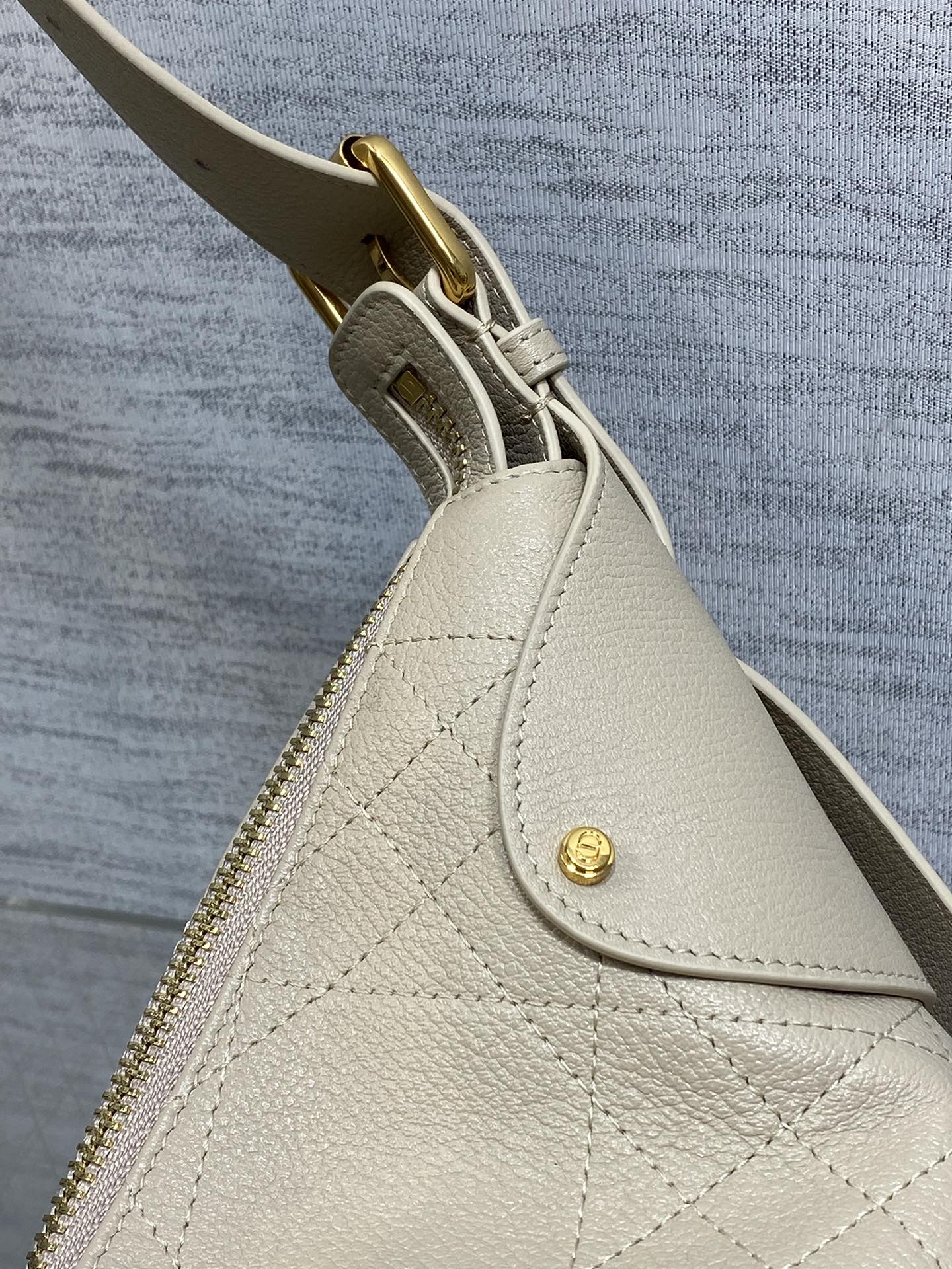 Cream leather bag corner with gold zipper pull and decorative stitching