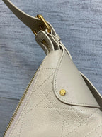 Cream leather bag side with gold zipper pull and small round logo snap detail.