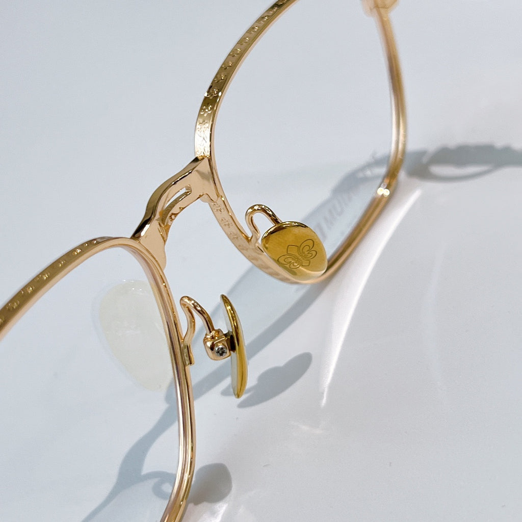 Gold eyeglasses temple close-up with small heart emblem on frame.