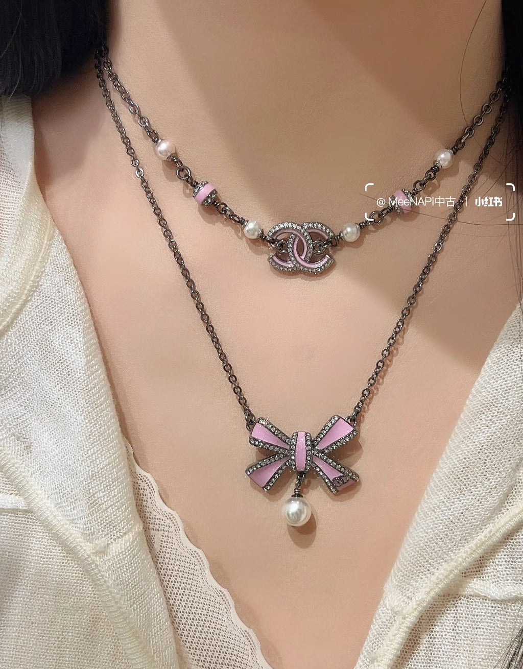Silver layered necklace on model, featuring ribbon bow, pearl drops, and logo charm