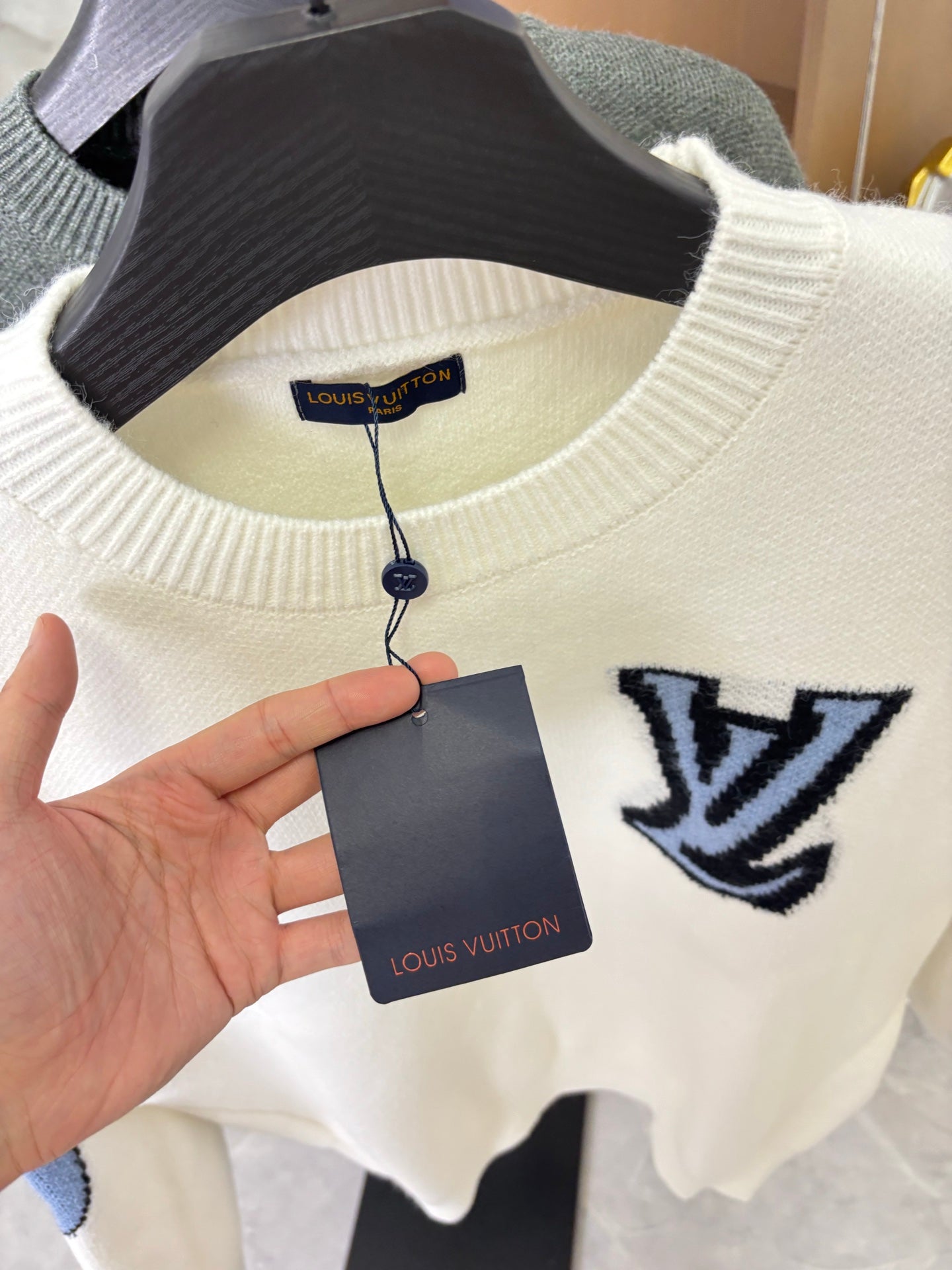 Off-white knit sweater with navy LV logo; tag hanging from collar