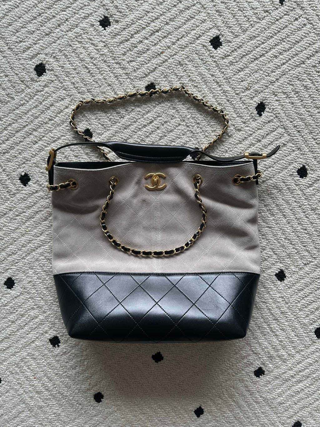 Two-tone tote bag with chain handles; light top, black base, gold logo charm