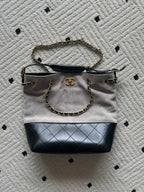 Two-tone tote bag with chain handles; light top, black base, gold logo charm