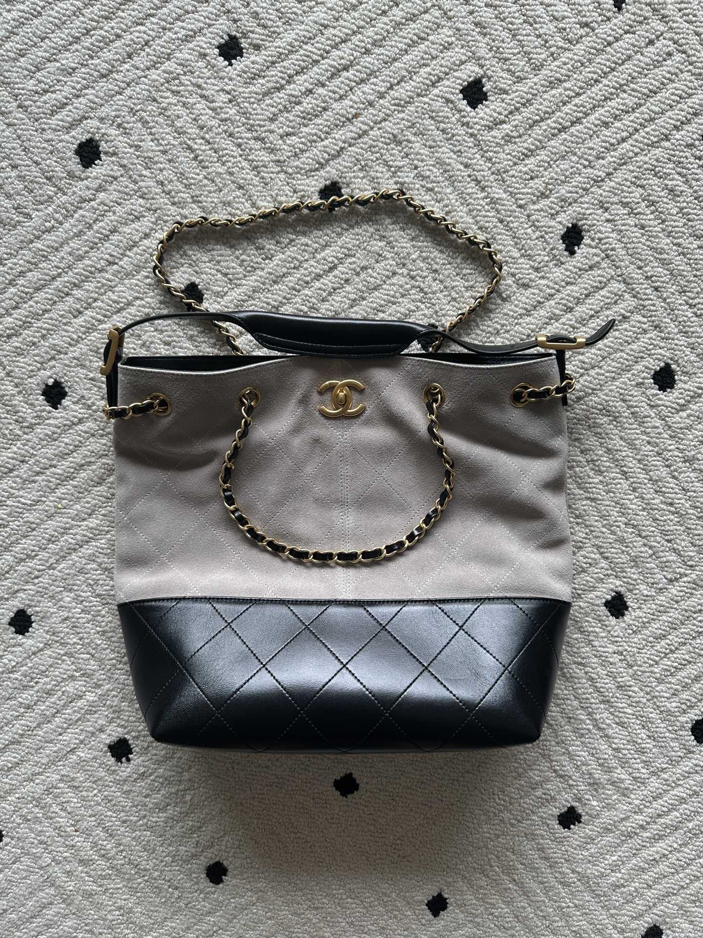 Two-tone tote bag with chain handles; light top, black base, gold logo charm