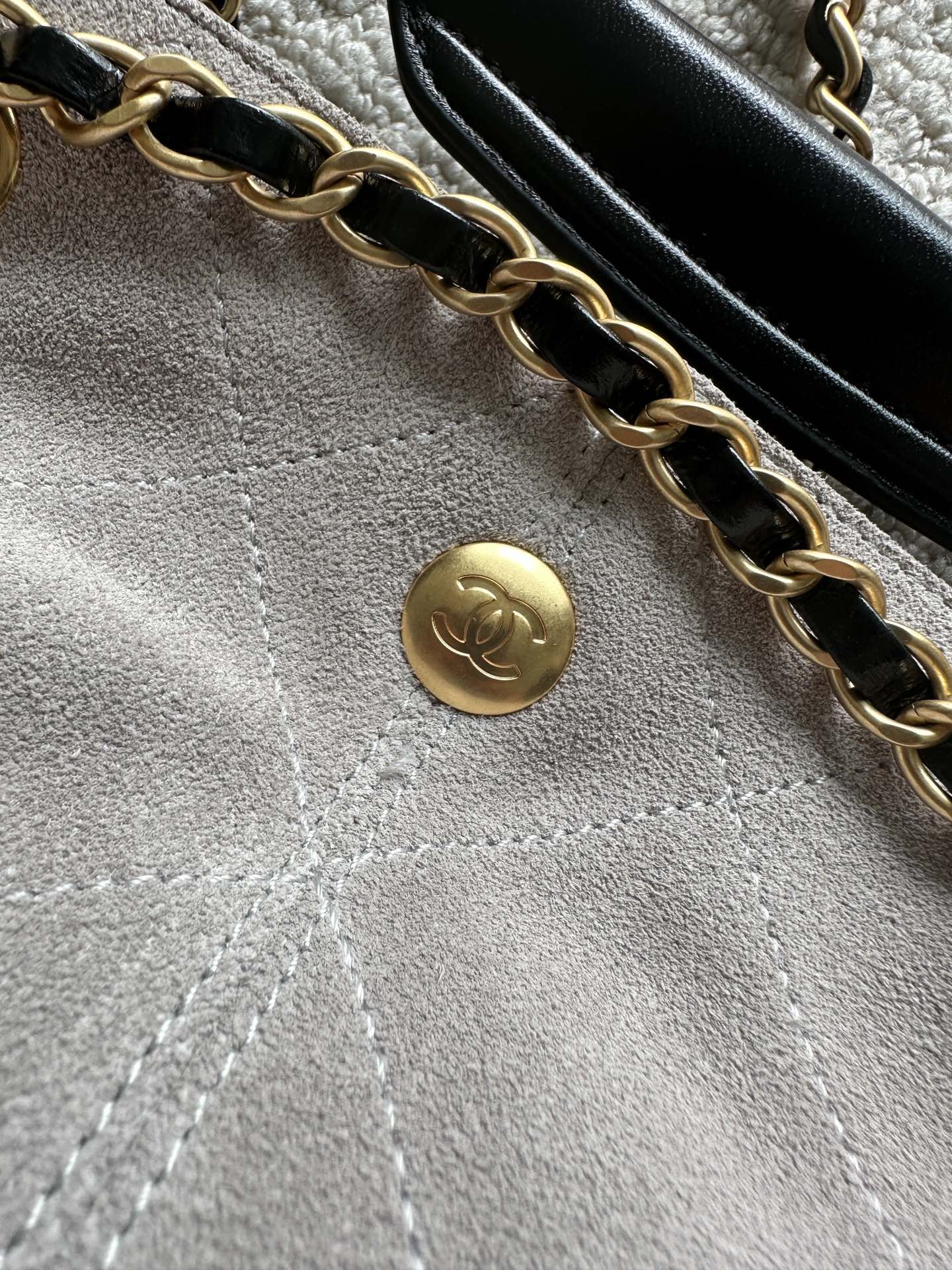 Gold chain and small round Chanel emblem on light fabric interior