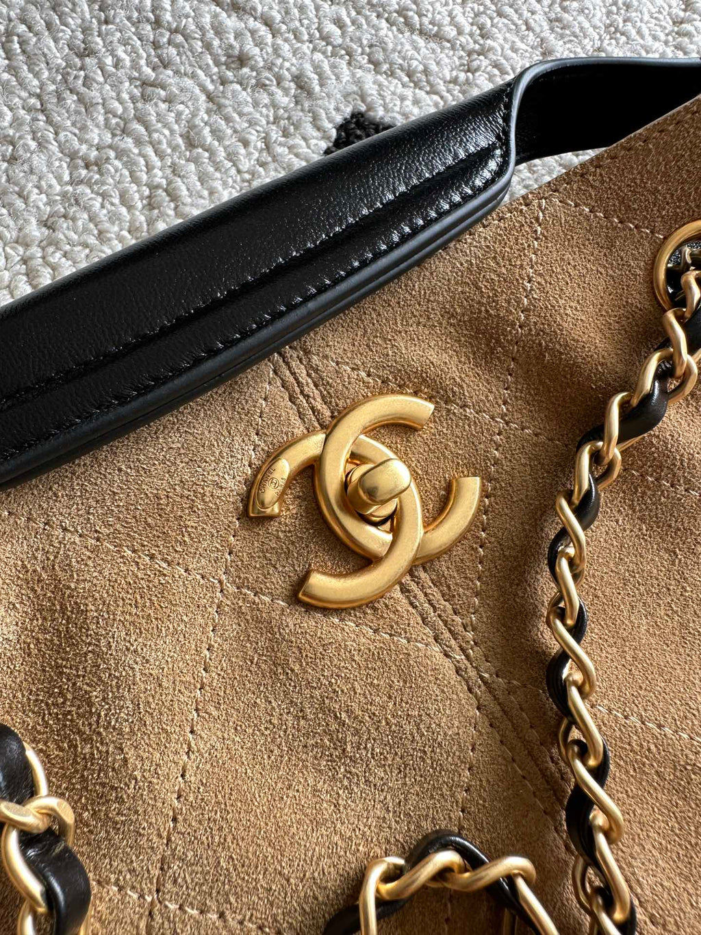 Chanel logo detail on tan fabric front of two-tone handbag with black leather trim.