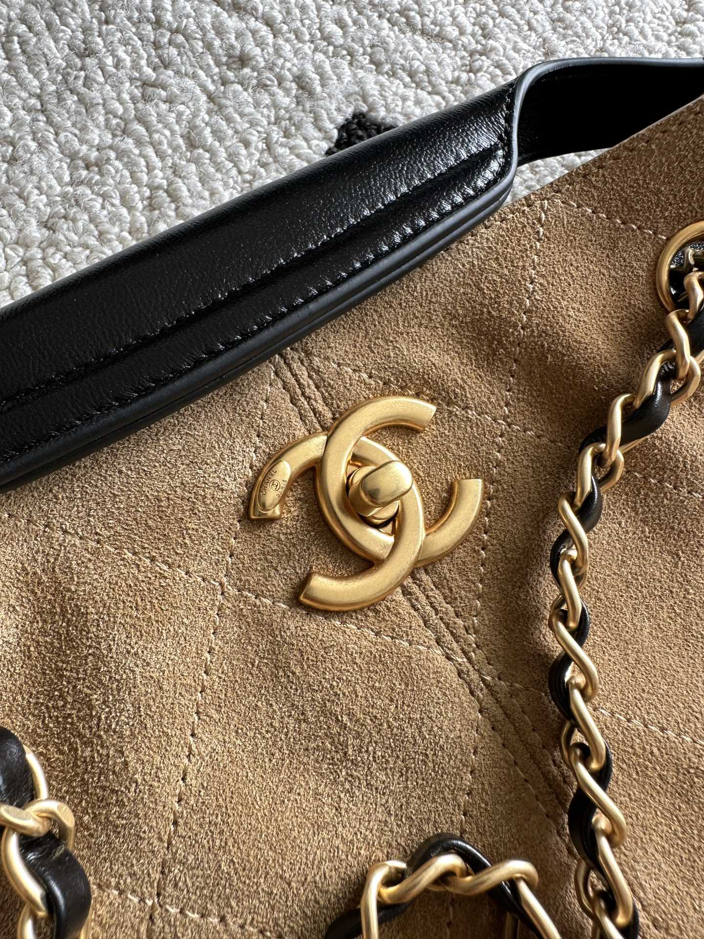 Chanel logo detail on tan fabric front of two-tone handbag with black leather trim.
