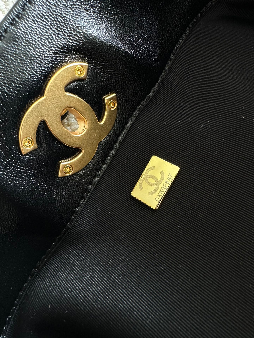 Black leather handbag close-up with gold CC logo emblem and small fabric tag.