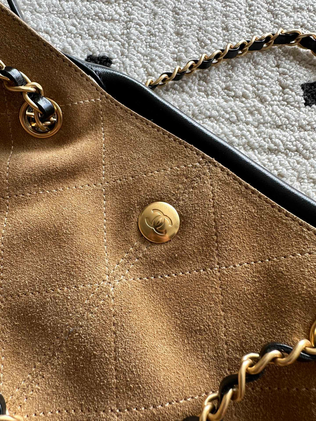 Two-tone handbag front close-up with round gold snap button and gold chain strap.