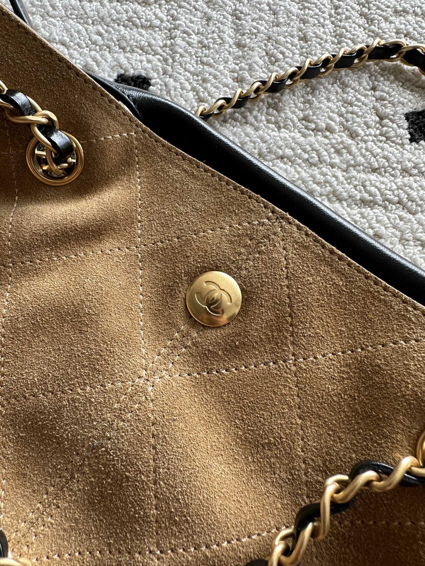 Two-tone handbag front close-up with round gold snap button and gold chain strap.