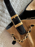 Beige fabric handbag with black leather strap tab and gold chain, CHANEL hardware label.