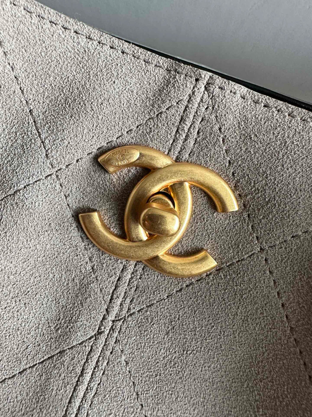 Chanel handbag CC metal logo on taupe leather, close-up detail.