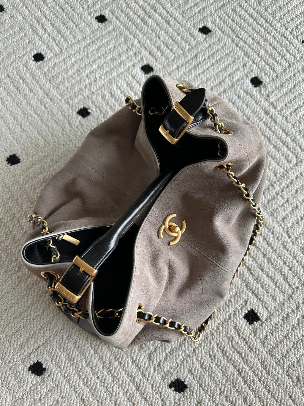 Chanel handbag laid flat in taupe and black, top open with chain strap and CC emblem.