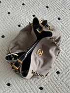 Chanel handbag laid flat in taupe and black, top open with chain strap and CC emblem.