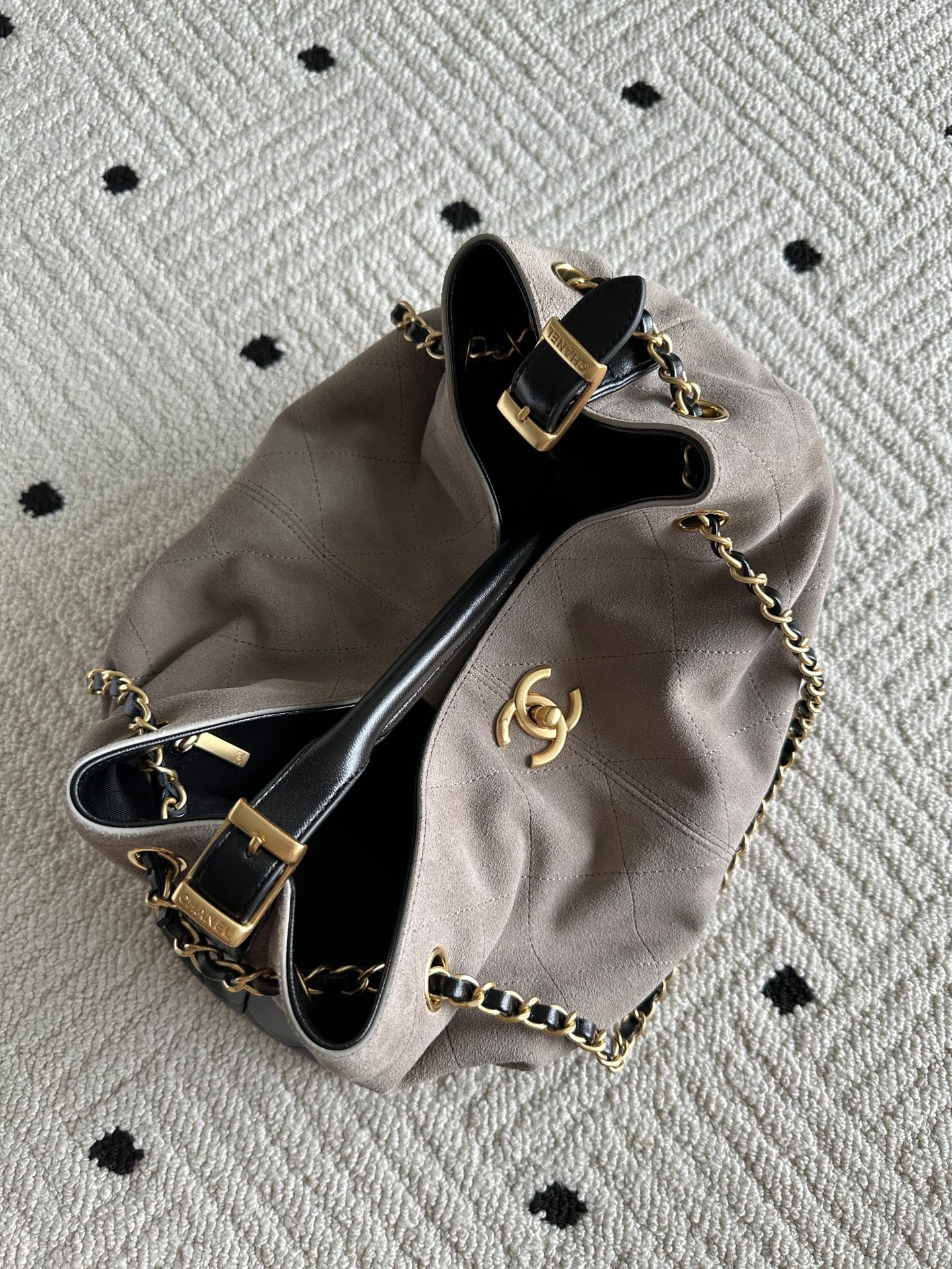 Chanel handbag laid flat in taupe and black, top open with chain strap and CC emblem.