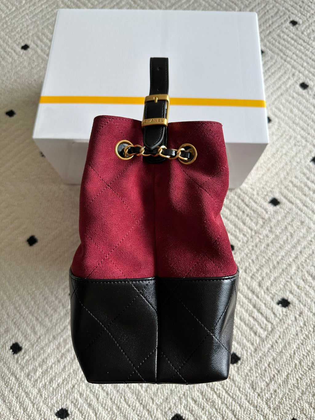 Burgundy and black drawstring-style handbag with gold-tone hardware on top