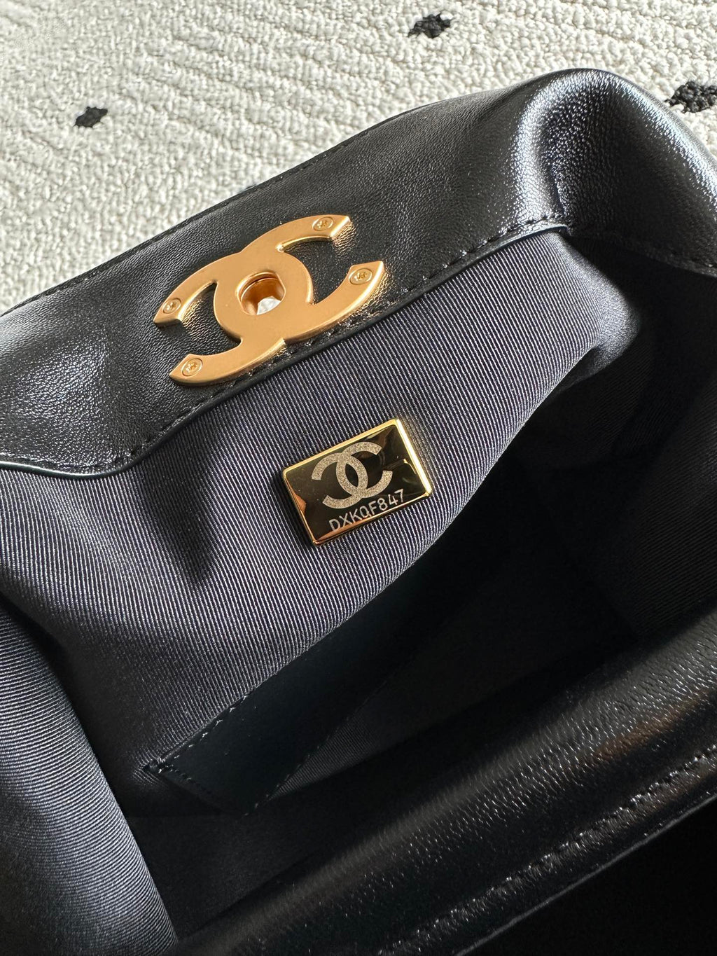Black bag flap with gold Chanel logo plate on an interior panel of a two-tone shoulder bag.