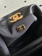Black bag flap with gold Chanel logo plate on an interior panel of a two-tone shoulder bag.