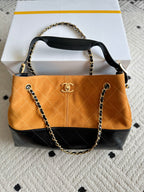 Two-tone shoulder bag with gold chain strap; orange front panel and Chanel emblem center.