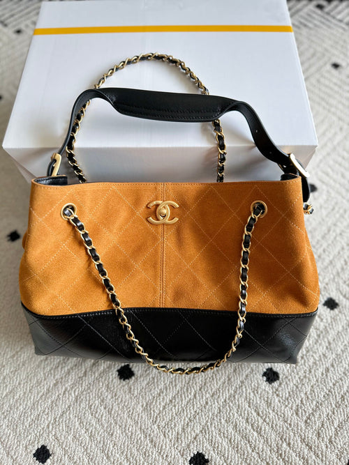 Two-tone shoulder bag with gold chain strap; orange front panel and Chanel emblem center.