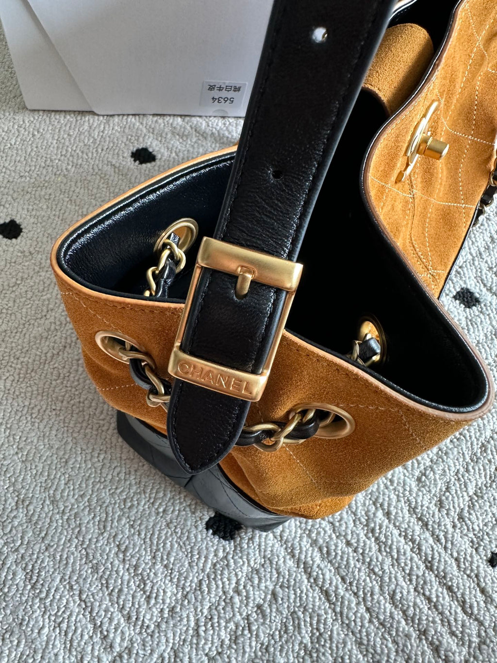 Black strap with gold buckle and chain hardware on an orange-and-black two-tone bag.