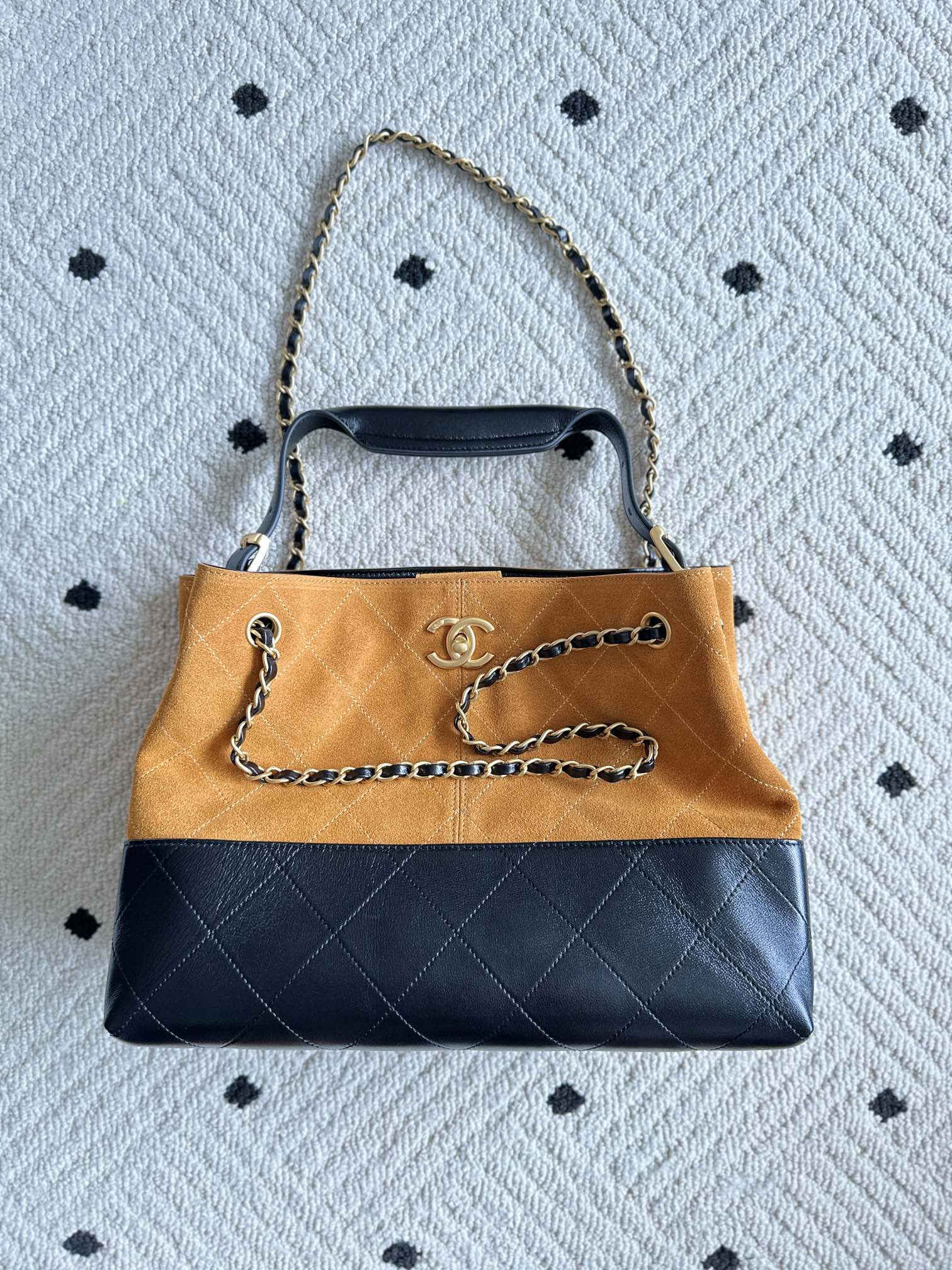 Two-tone shoulder bag, orange top and dark bottom, gold chain strap and handle grips.