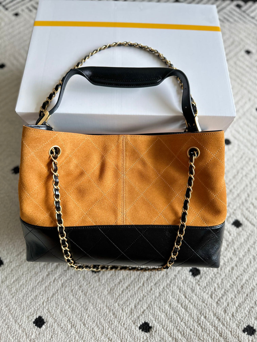 Two-tone shoulder bag with orange quilted front, dark lower panel, and gold chain handles.