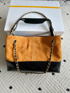 Two-tone shoulder bag with orange quilted front, dark lower panel, and gold chain handles.