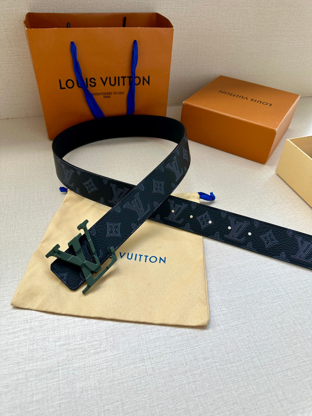 Monogram belt with dark blue strap and green buckle, extended strap end
