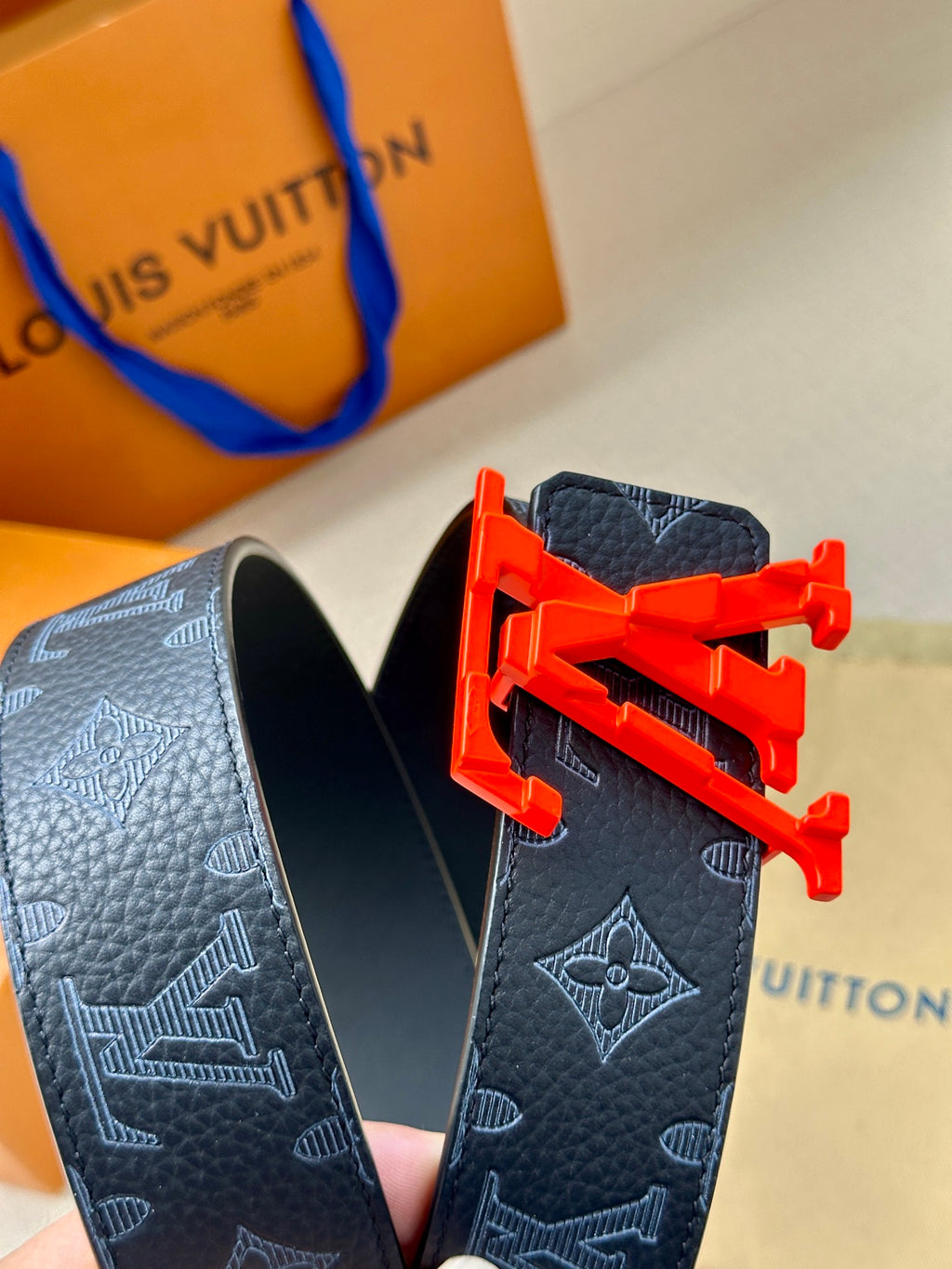 Louis Vuitton belt buckle closeup on dark monogram strap with red LV emblem