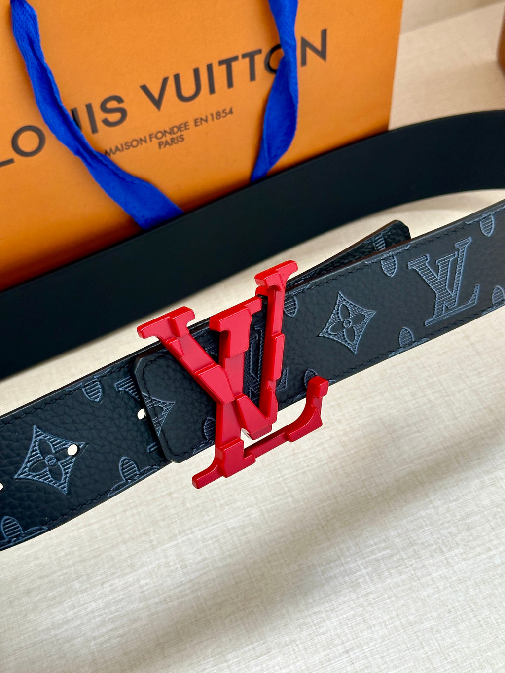 Louis Vuitton belt close-up: dark monogram strap with red LV buckle centerpiece
