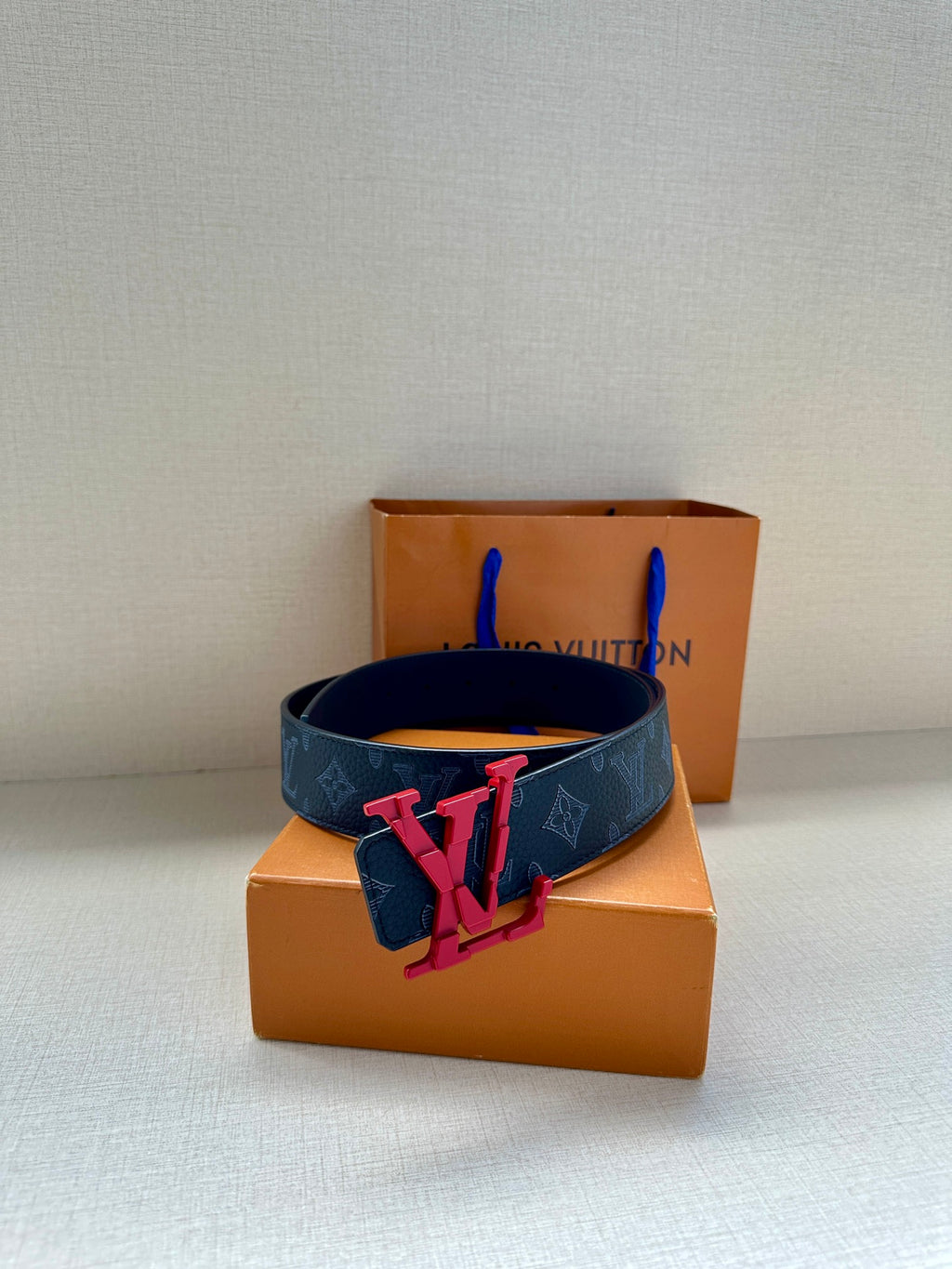 Louis Vuitton belt with dark monogram strap and red V emblem buckle on box