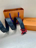 Louis Vuitton belt with dark monogram strap, red buckle hardware, laid on surface