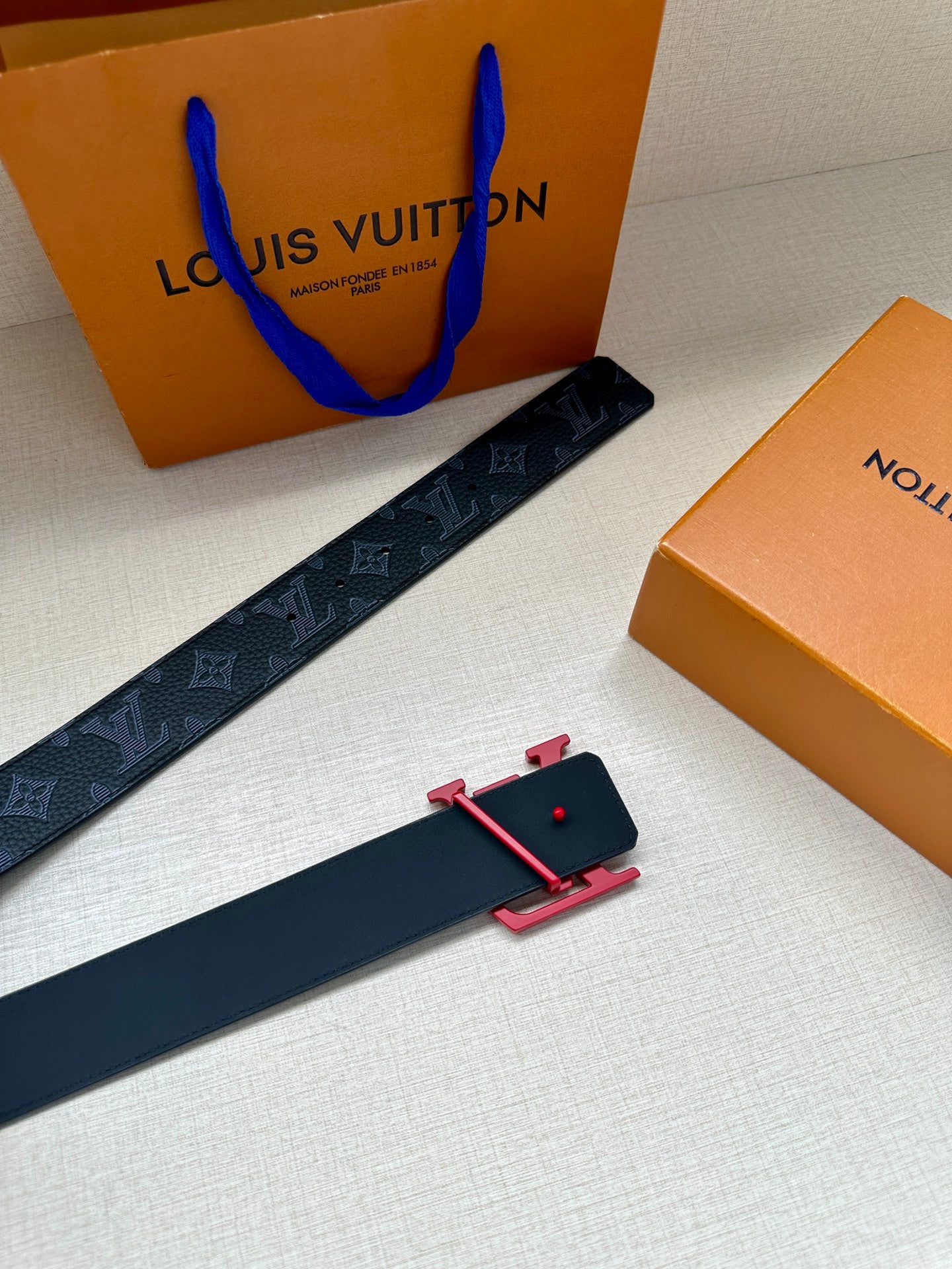 Louis Vuitton belt with dark monogram strap and red buckle with black keeper piece