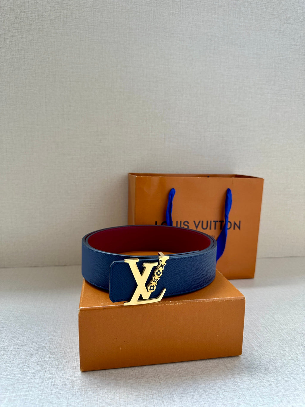 Louis Vuitton belt with navy blue strap and contrasting red underside, on boxes