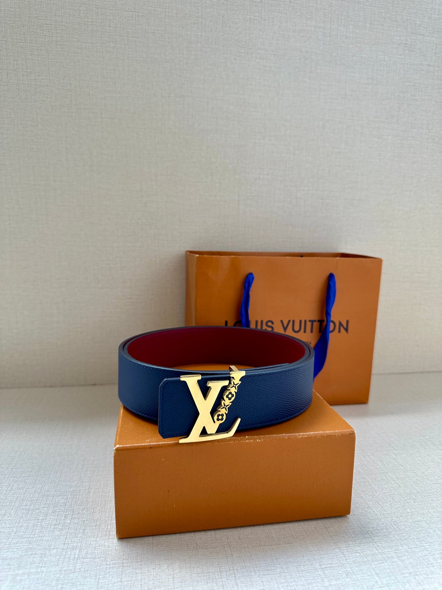 Louis Vuitton belt with navy blue strap and contrasting red underside, on boxes
