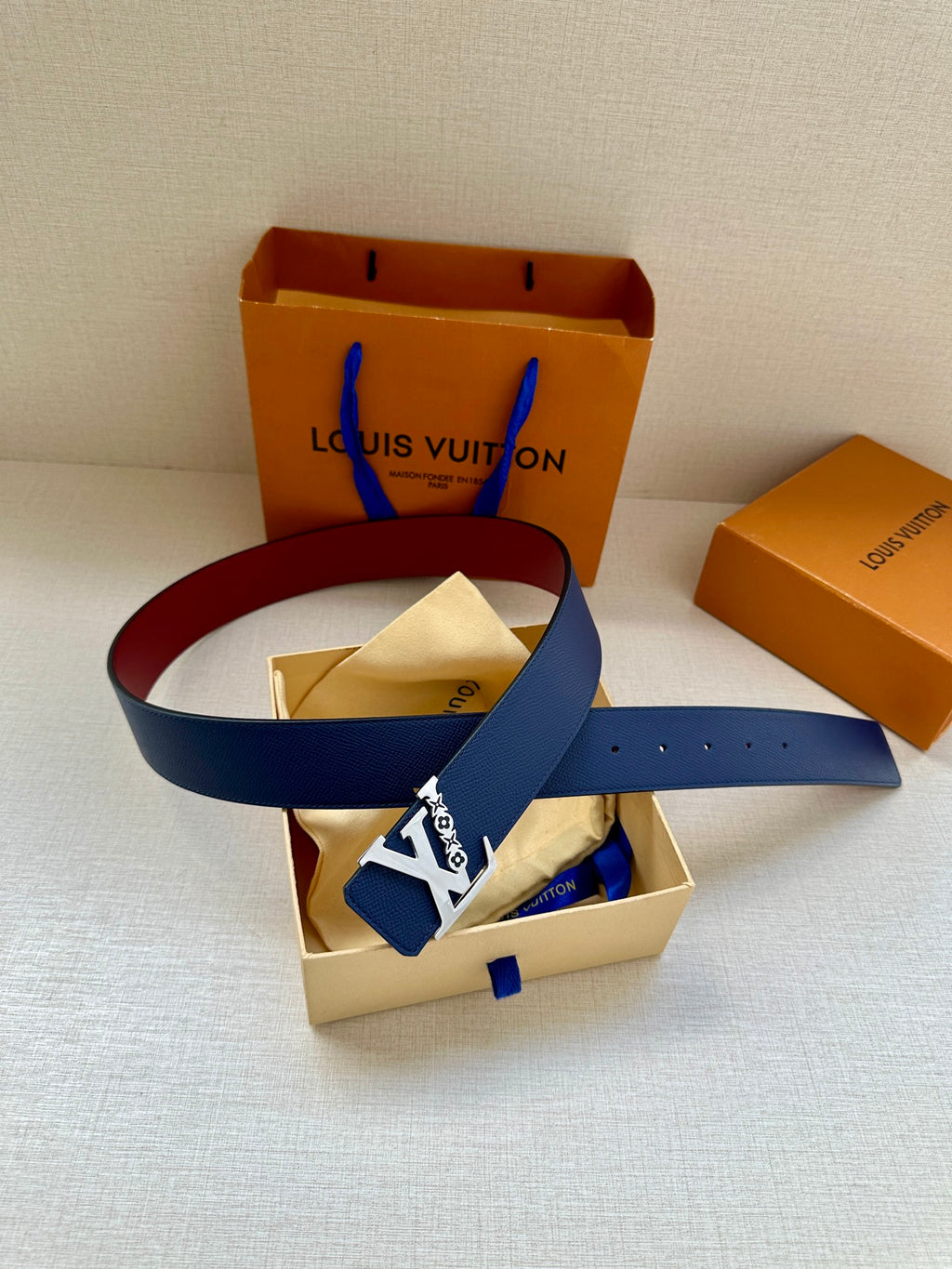 Louis Vuitton belt with navy blue strap and LV buckle, laid across gift boxes