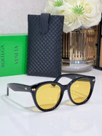 Black round sunglasses with yellow-tinted lenses and textured black protective case