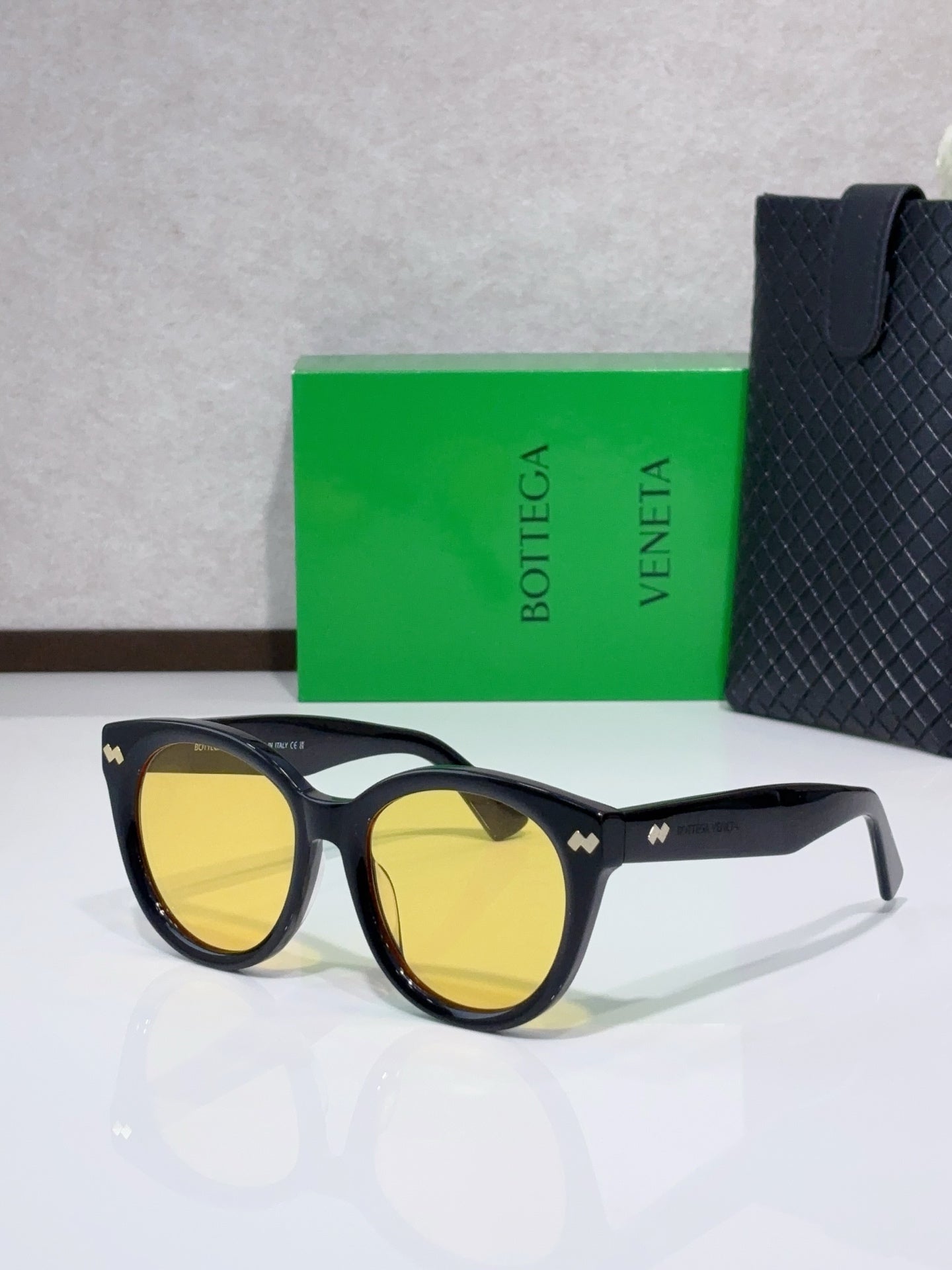Black round sunglasses with yellow-tinted lenses and logo detail at the bridge