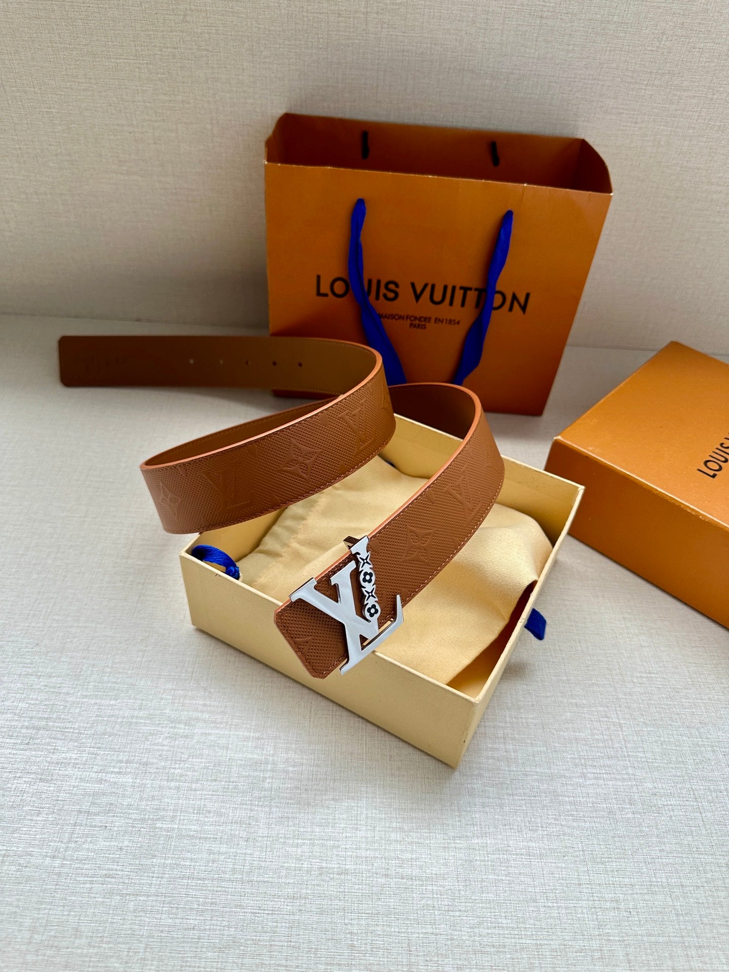 Louis Vuitton leather belt with tan strap and gold LV buckle, shown in open gift box