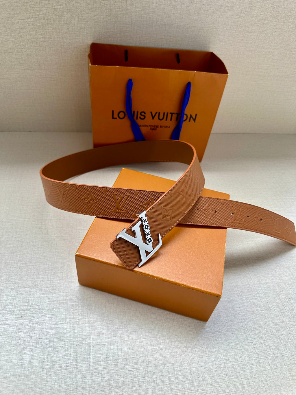 Louis Vuitton belt with tan leather strap and gold LV buckle, laid flat
